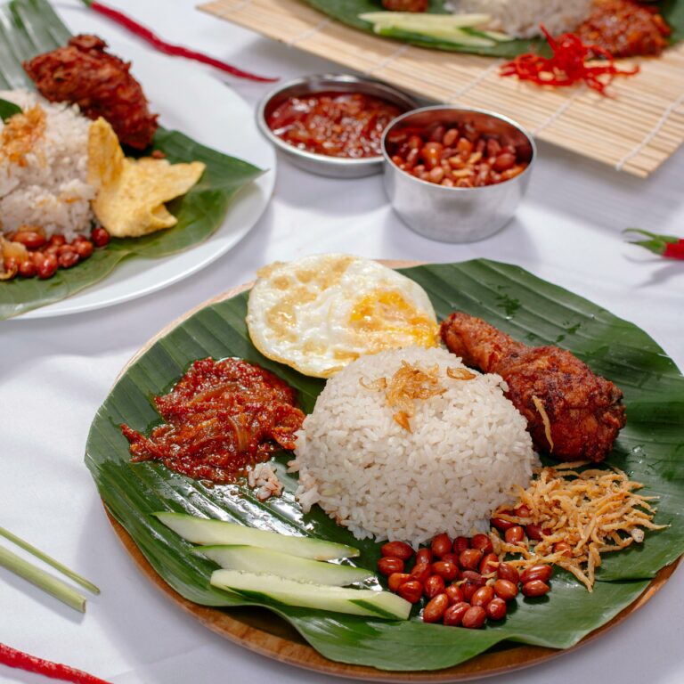 A delicious Nasi Lemak dish with rice, fried chicken, sambal, and garnishes served on banana leaf.