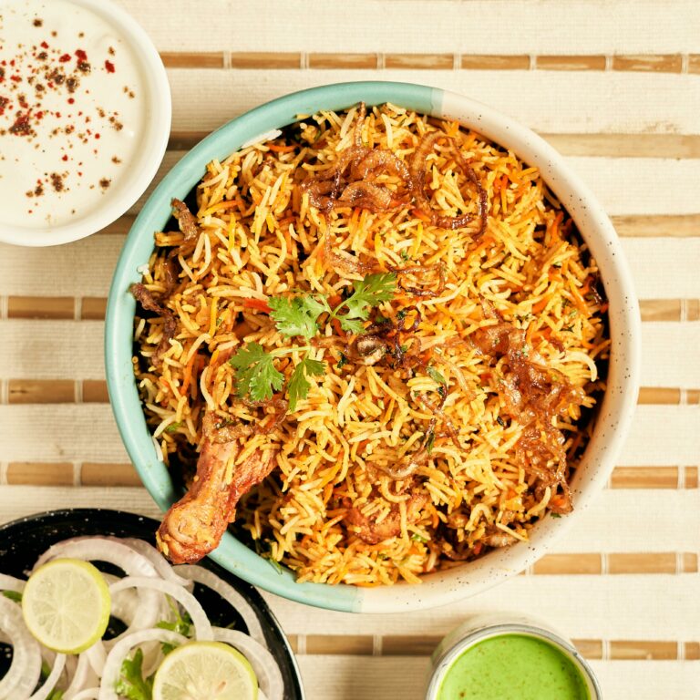 Delicious chicken biryani served with onion rings, lime, and yogurt dip, perfect for food lovers.