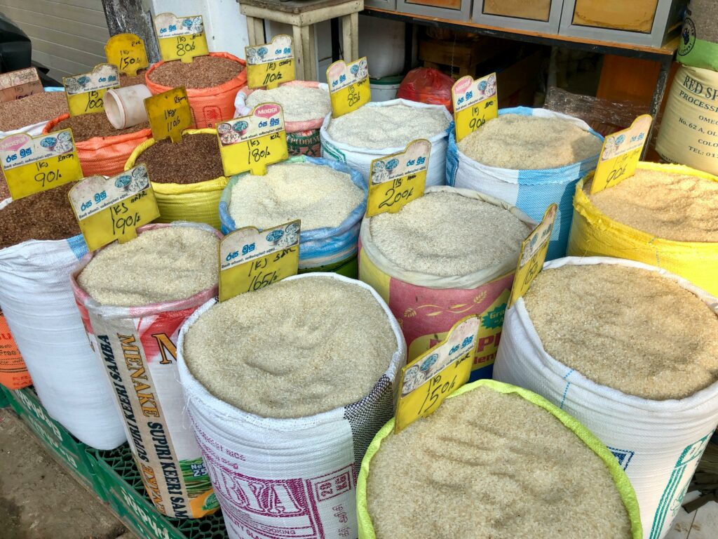 Different types of grains in bags with price tags at a bustling local market.